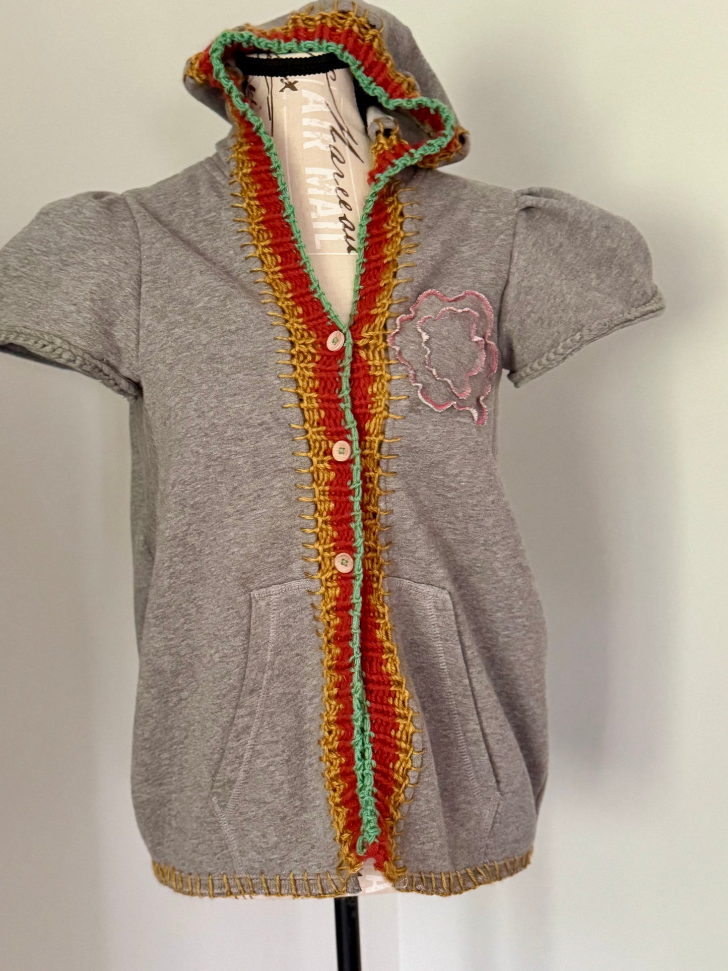 Upcycled gray hoodie trimmed with hand knitted stitch work in Gold, Red and Teal and features a layered hand cut flower made of repurposed sweatshirt fabric scraps.