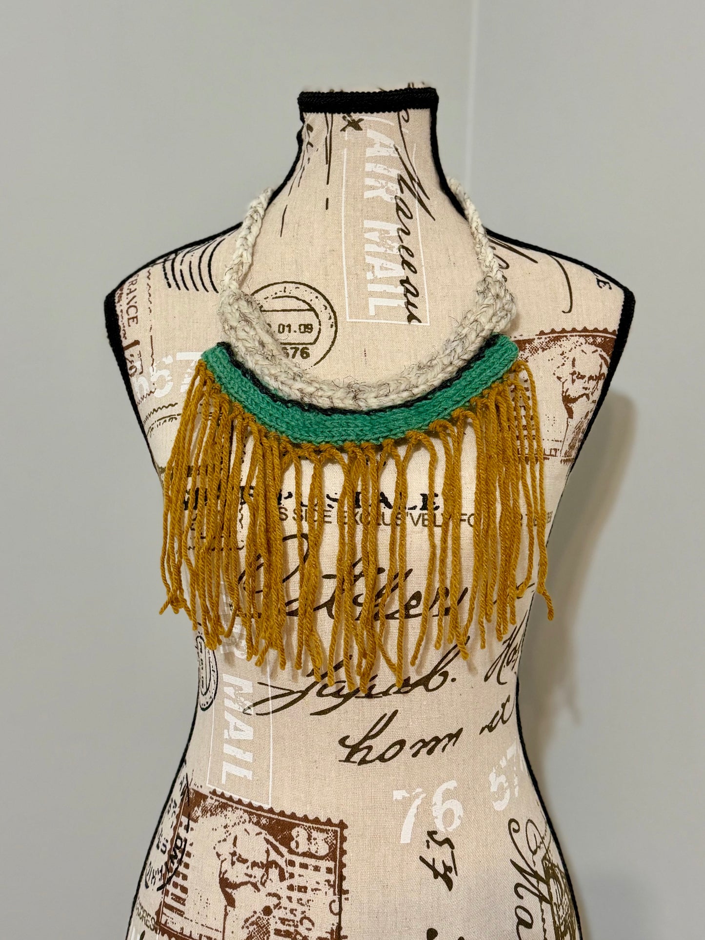 Hand knitted structured statement necklace in white, gold teal and black yarns featuring a dramatic fringed drape.