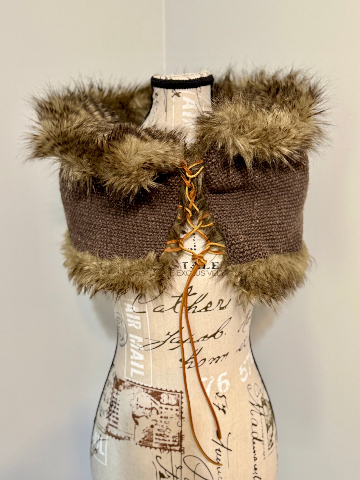 Brown knitted vest with faux fur trim and leather lacing on a mannequin against a plain background