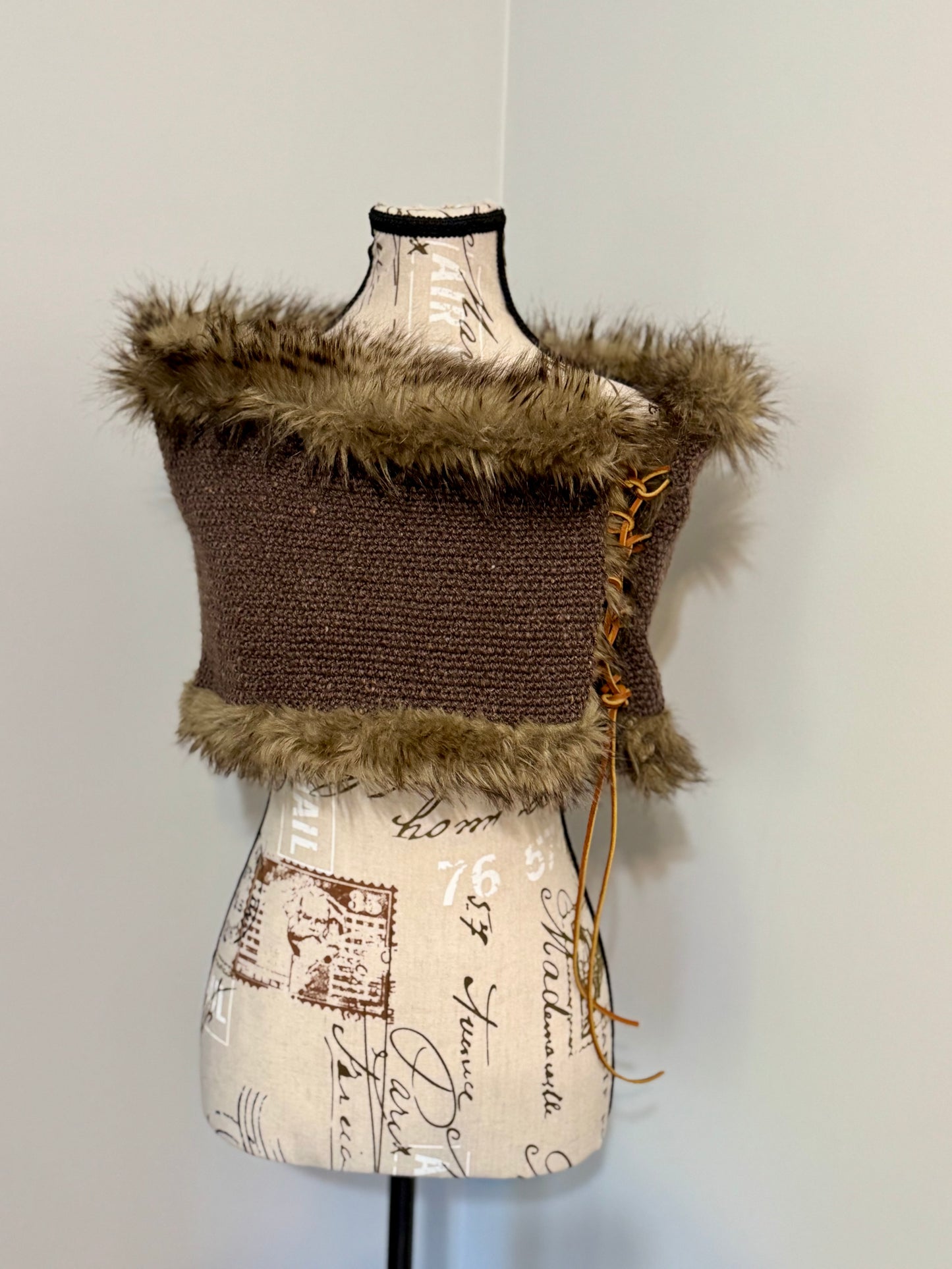 Brown knitted vest with faux fur trim and leather lacing on a mannequin against a plain background